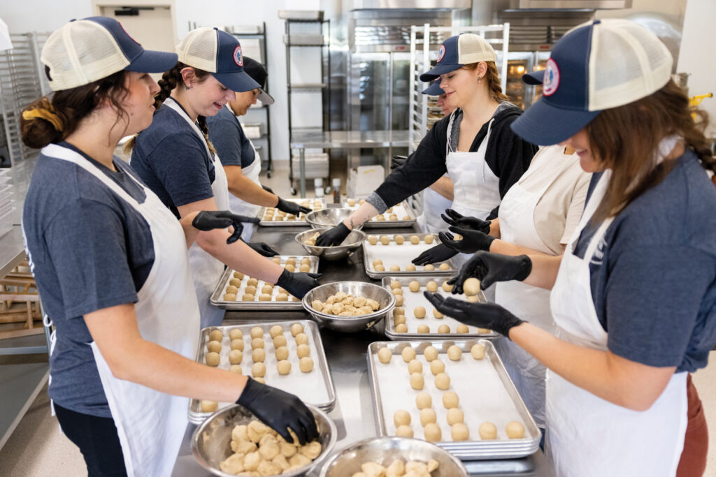 The production team rolls cookie dough; cookies are put into the oven