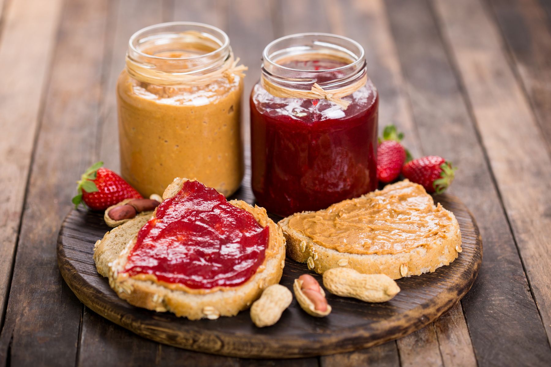 A peanut butter jelly sandwich on a plate with peanut butter and jelly in jars.