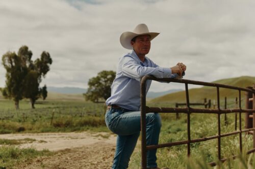 Photo of cowboy resting on fence