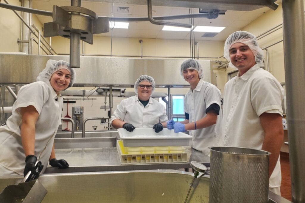 Four people smiling for camera in creamery room