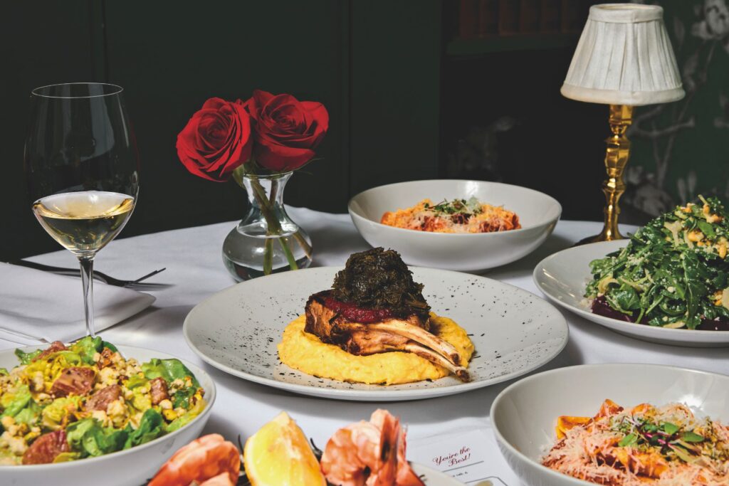 A feast set on the restaurant’s white tablecloth. The Niman Ranch bone-in pork chop, dressed in veal bordelaise, bacon-braised greens, and smoked tomato jam and paired with parmesan polenta, is front and center.